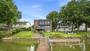 A modern house with a dock leading to a pond, surrounded by greenery and other houses. - MINNeSTAY* Lakefront Luxury (Mound)