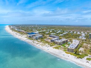 An aerial view of a coastal resort with beachfront properties, a sandy beach, and a clear blue sky.