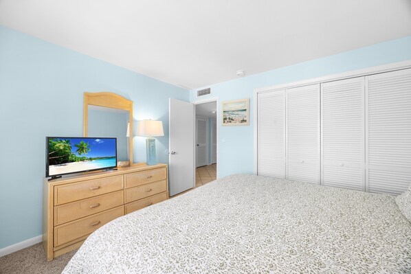 A bedroom with a bed, a dresser, a television, a mirror, and a closet.