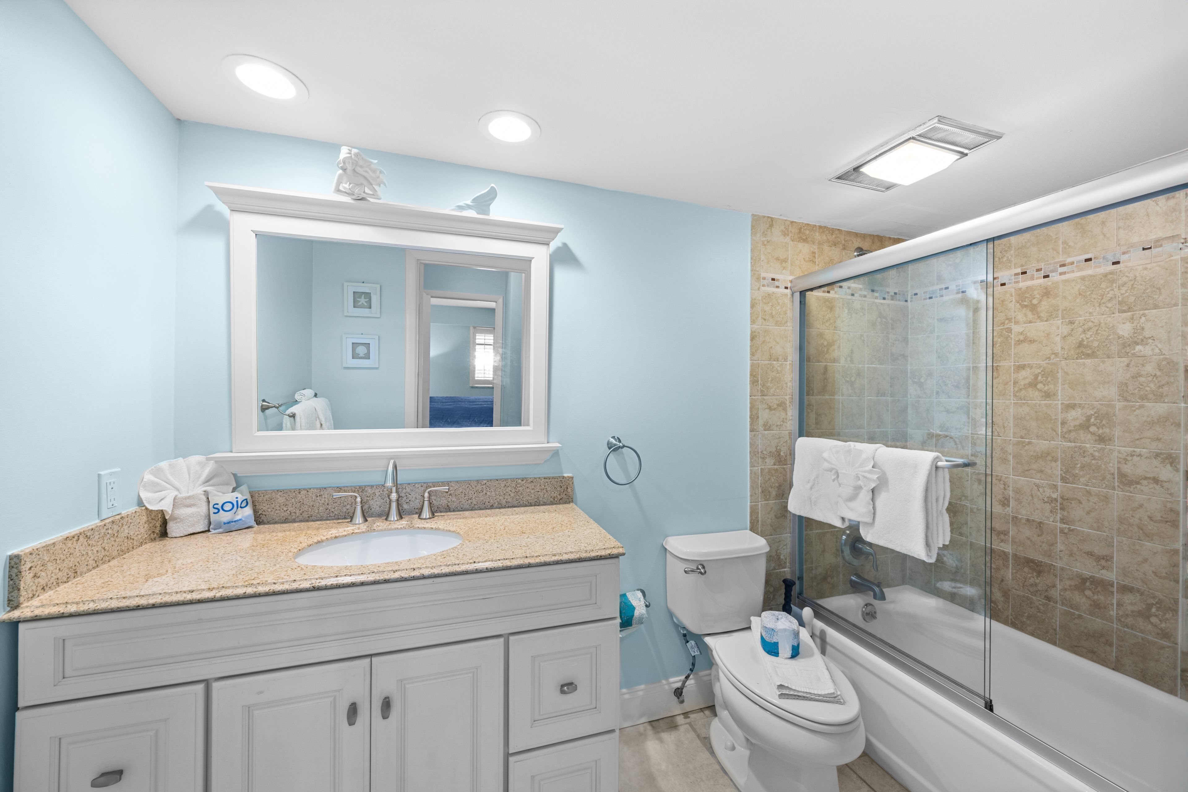 A bathroom with a sink, mirror, toilet, and shower area.