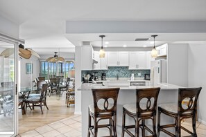 A modern kitchen with white cabinets, a large island, and a dining area with wicker chairs.