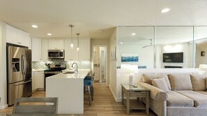A modern kitchen with stainless steel appliances, a central island, and a dining area with a sofa and table. - Stunning Ocean, Pool, and Garden views from Beautifully Appointed Unit! (Oceanside)