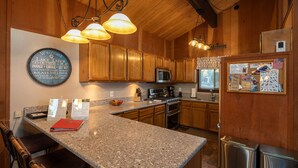 A kitchen with granite countertops, wooden cabinets, a stainless steel refrigerator, and a microwave. - Grainger by Hauserman Rental Group (Tahoe City)