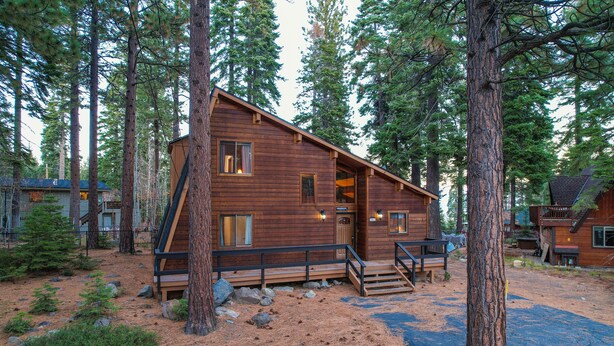 A wooden cabin with a deck, surrounded by tall trees. - Grainger by Hauserman Rental Group (Tahoe City)