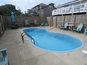 A backyard with a swimming pool, patio furniture, and a wooden fence.
