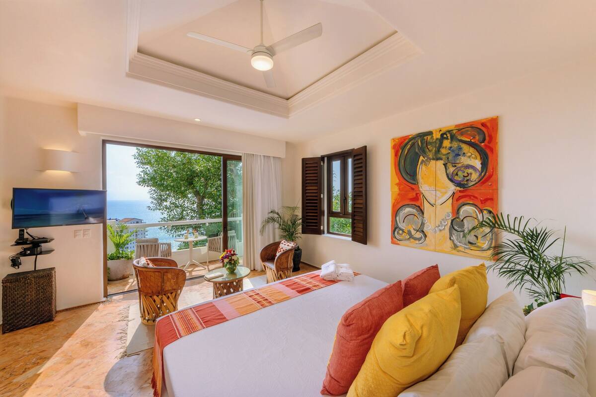 Ein Hotelzimmer mit Bett, Fernseher, einem Balkon mit Blick und einem Bild an der Wand.