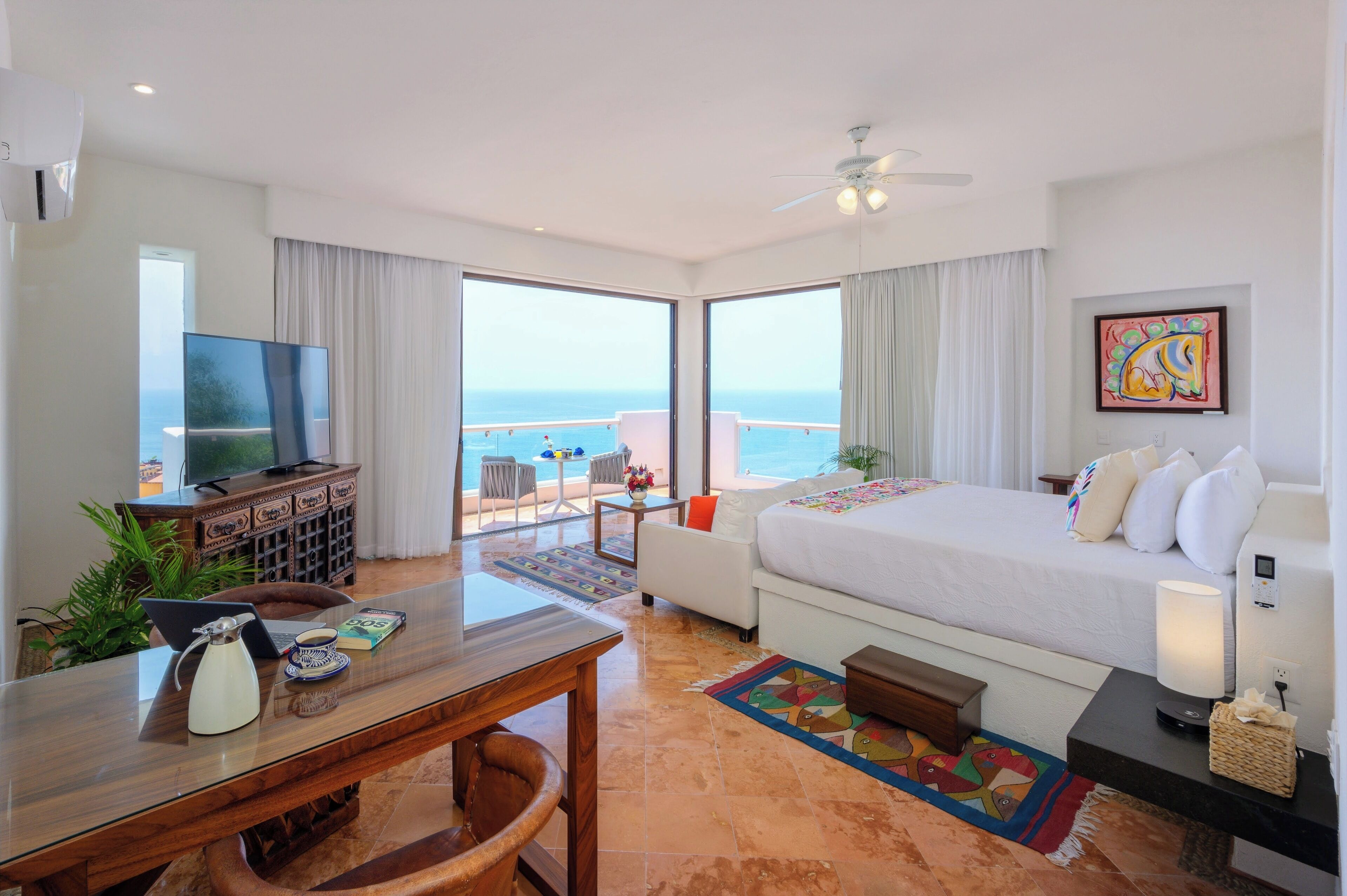 Una habitación de hotel con cama, escritorio, computadora portátil, televisor y vista al océano.