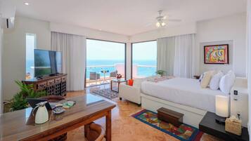 Una habitación de hotel con cama, escritorio, computadora portátil, televisor y vista al océano.