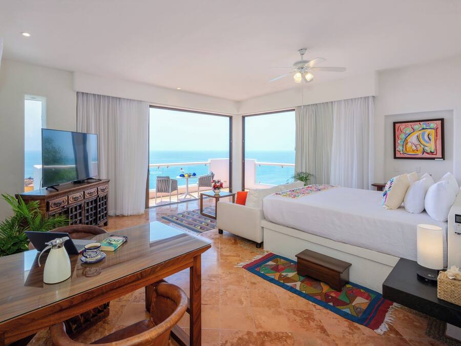 Una habitación de hotel con cama, escritorio, computadora portátil, televisor y vista al océano.