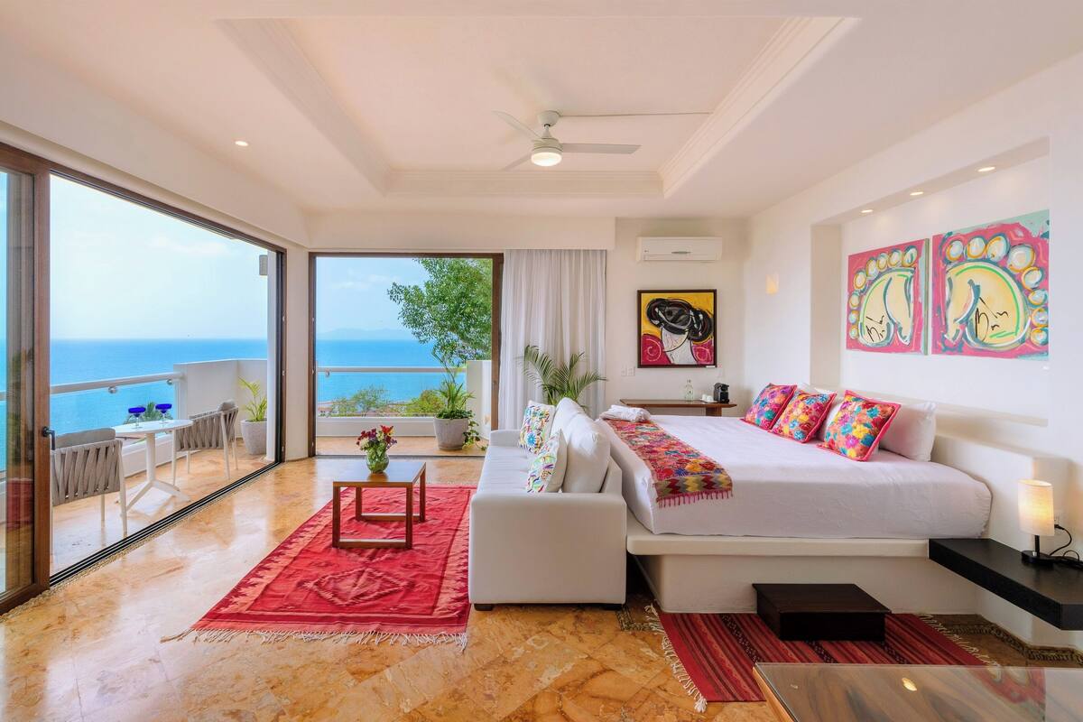 Ein Schlafzimmer mit Bett, einer Couch, einem kleinen Tisch und einem Balkon mit Meerblick.