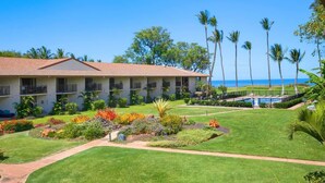 A hotel with a pool, a well-maintained lawn, and a view of the ocean.