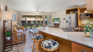 A modern kitchen with a central island, bar stools, and a dining area with outdoor views.