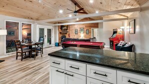Une pièce spacieuse équipée d’une table de billard, d’un plafond en bois et d’un coin repas avec une table et des chaises.