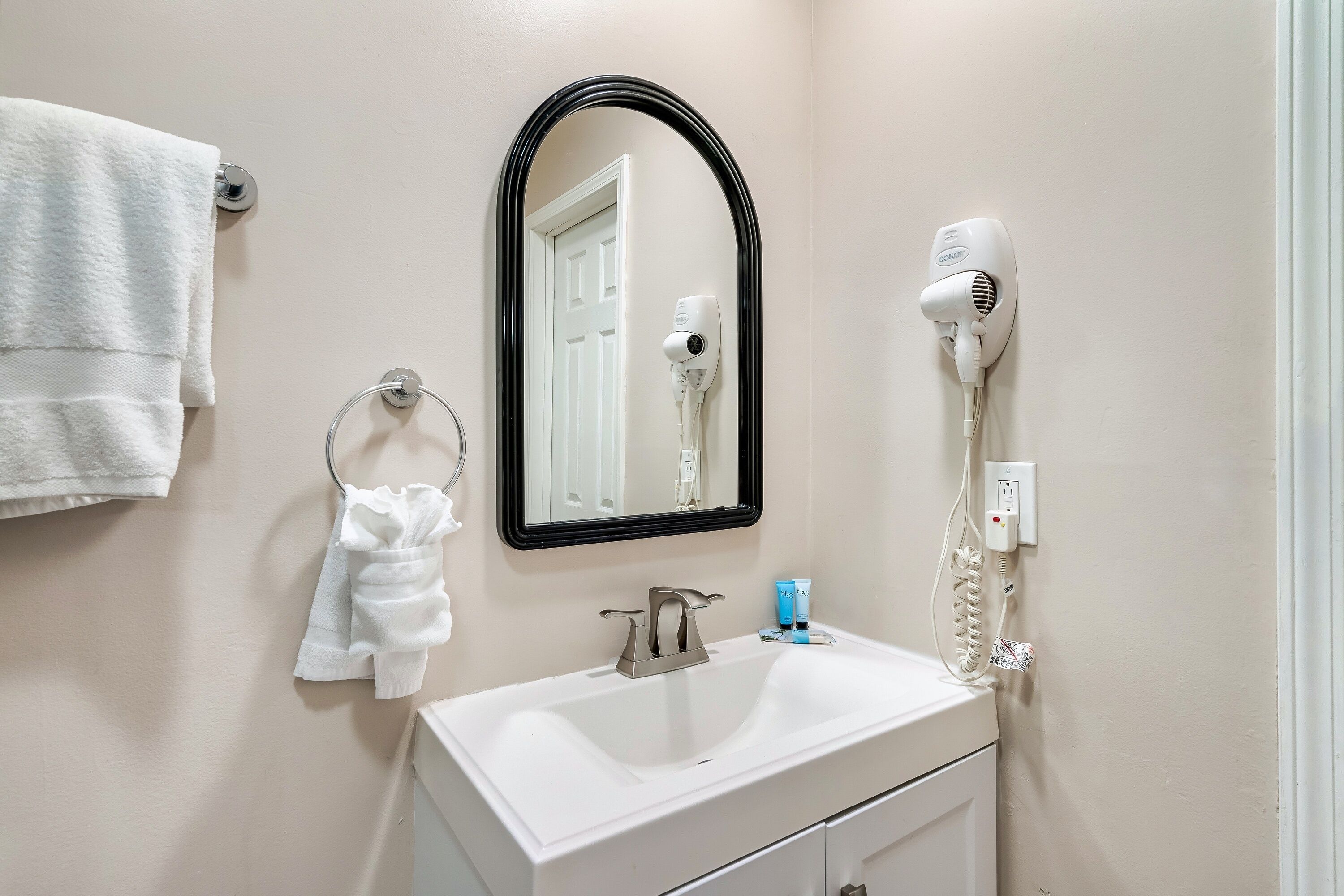 Un baño con un lavabo blanco, un espejo, un secador de pelo y un perchero para toallas.
