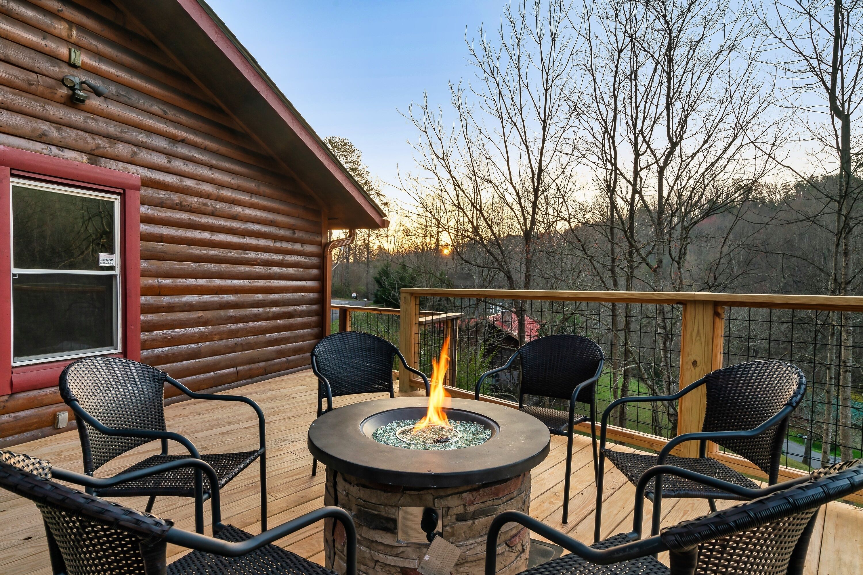 A log cabin with a deck featuring a stone fire pit surrounded by four wicker chairs.
