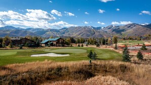 Un campo de golf con un club de campo, rodeado de montañas y edificios residenciales.