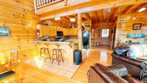 A cozy cabin interior with wooden walls, a kitchen area, a dining space, and a living room with a leather sofa. - Nature's View, Beautiful 3-Story Cabin; 3 Bdrms w/King Beds; Free WiFi (Sevierville)