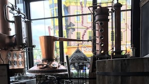A distillery interior with large copper stills, a stone wall, and a view of a colorful building outside. - Nature's View, Beautiful 3-Story Cabin; 3 Bdrms w/King Beds; Free WiFi (Sevierville)