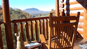 A wooden deck with a chair and a table, a wooden fence, and a view of a mountain range. - Nature's View, Beautiful 3-Story Cabin; 3 Bdrms w/King Beds; Free WiFi (Sevierville)