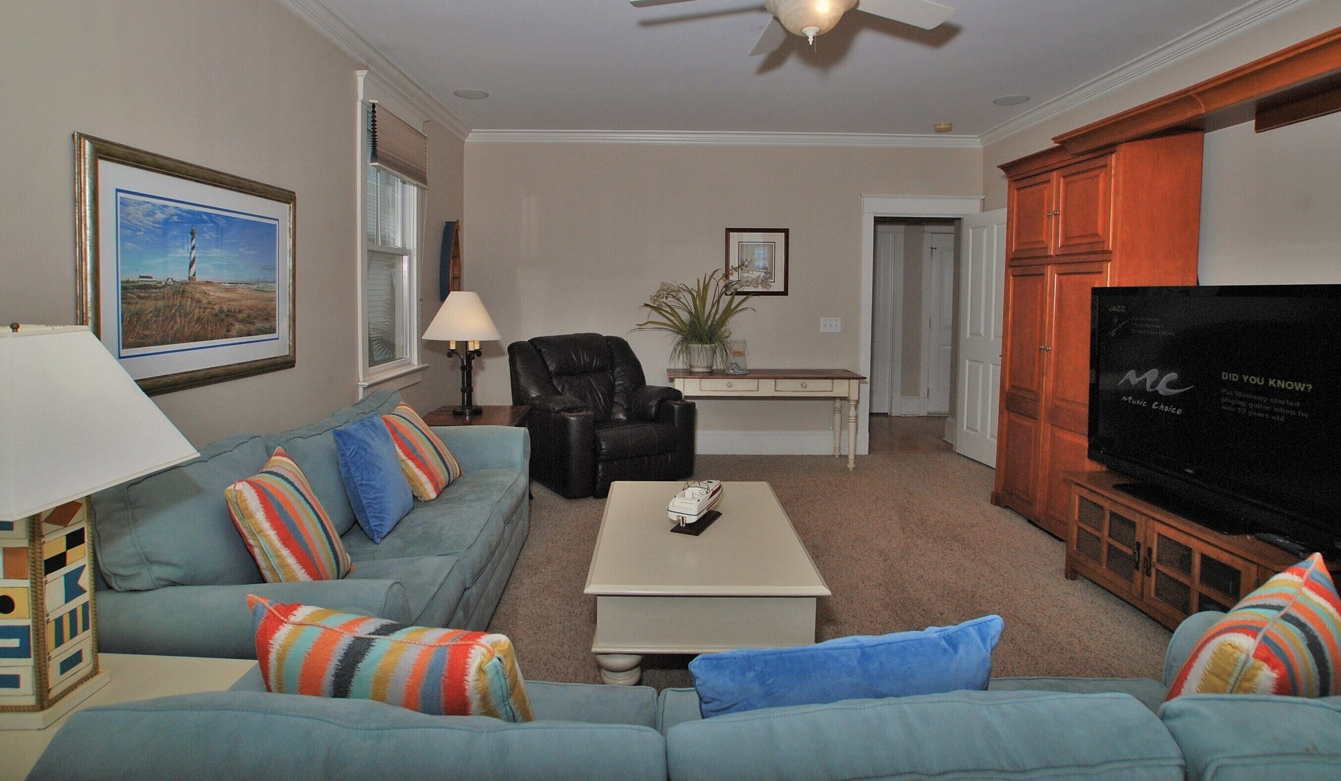 A living room with a sofa, armchair, coffee table, television, and a ceiling fan.