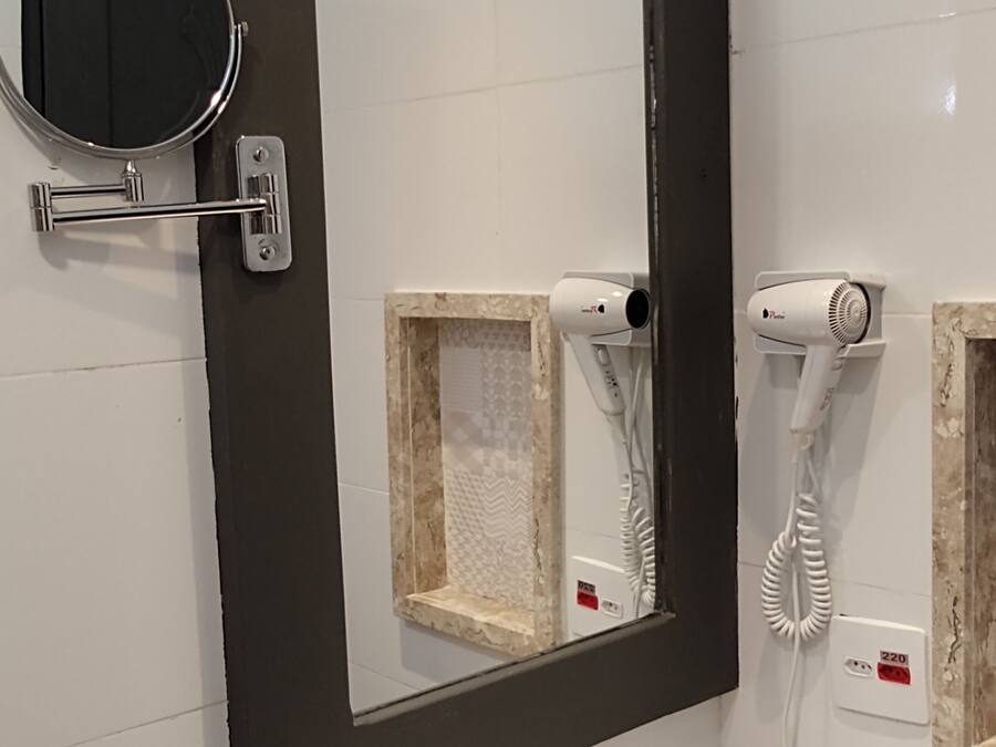 Un baño con un lavabo blanco, un espejo y dos secadores de pelo fijados a la pared.