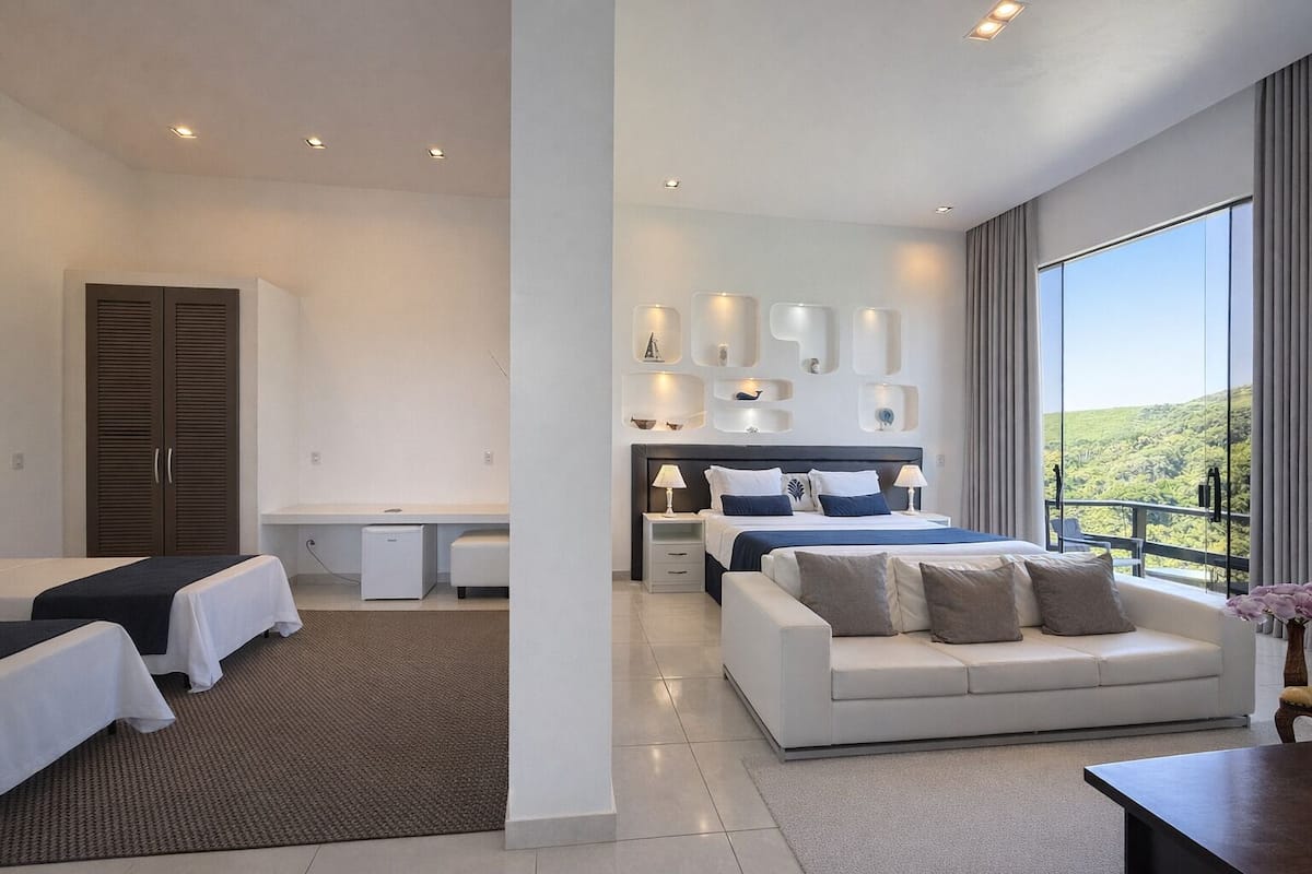 Habitació d'hotel moderna amb un llit gran, un sofà, una taula de treball i vistes a l'exterior.