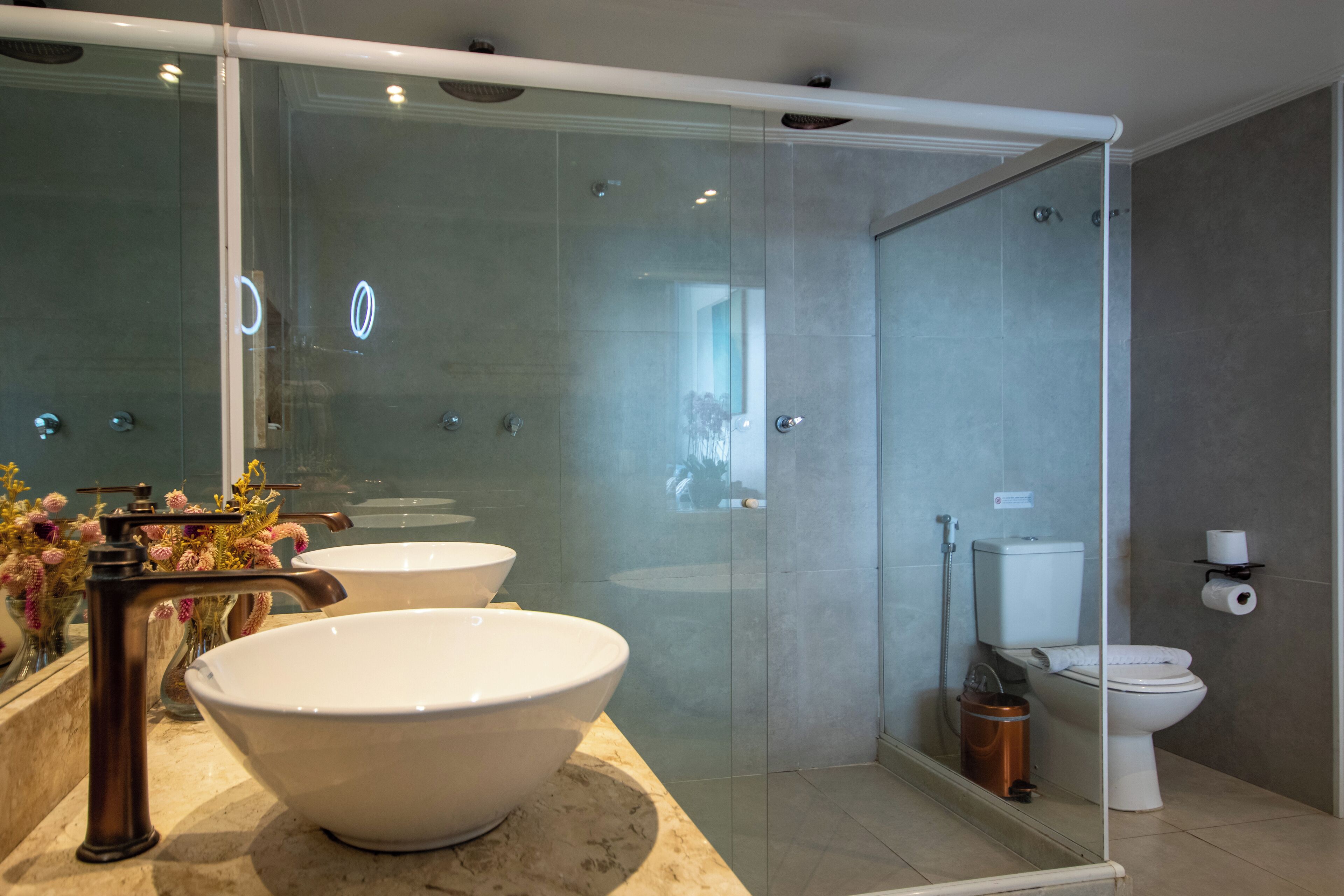 A modern bathroom with a large white sink, a glass-enclosed shower, and a toilet.