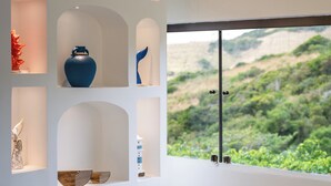 Un dormitorio moderno con una cama grande, vistas a zonas verdes a través de una ventana y objetos decorativos en estantes.