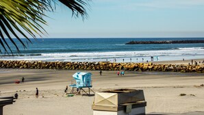 Une plage avec une tour de surveillance pour les sauveteurs, une digue rocheuse et un ciel dégagé.