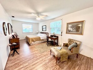 Relax in a spacious room with a large bed, desk, and armchair, surrounded by framed pictures and natural light.