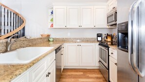Eine moderne Küche mit weißen Schränken, Granitarbeitsplatten, einem Edelstahlkühlschrank und einem eingebauten Backofen.