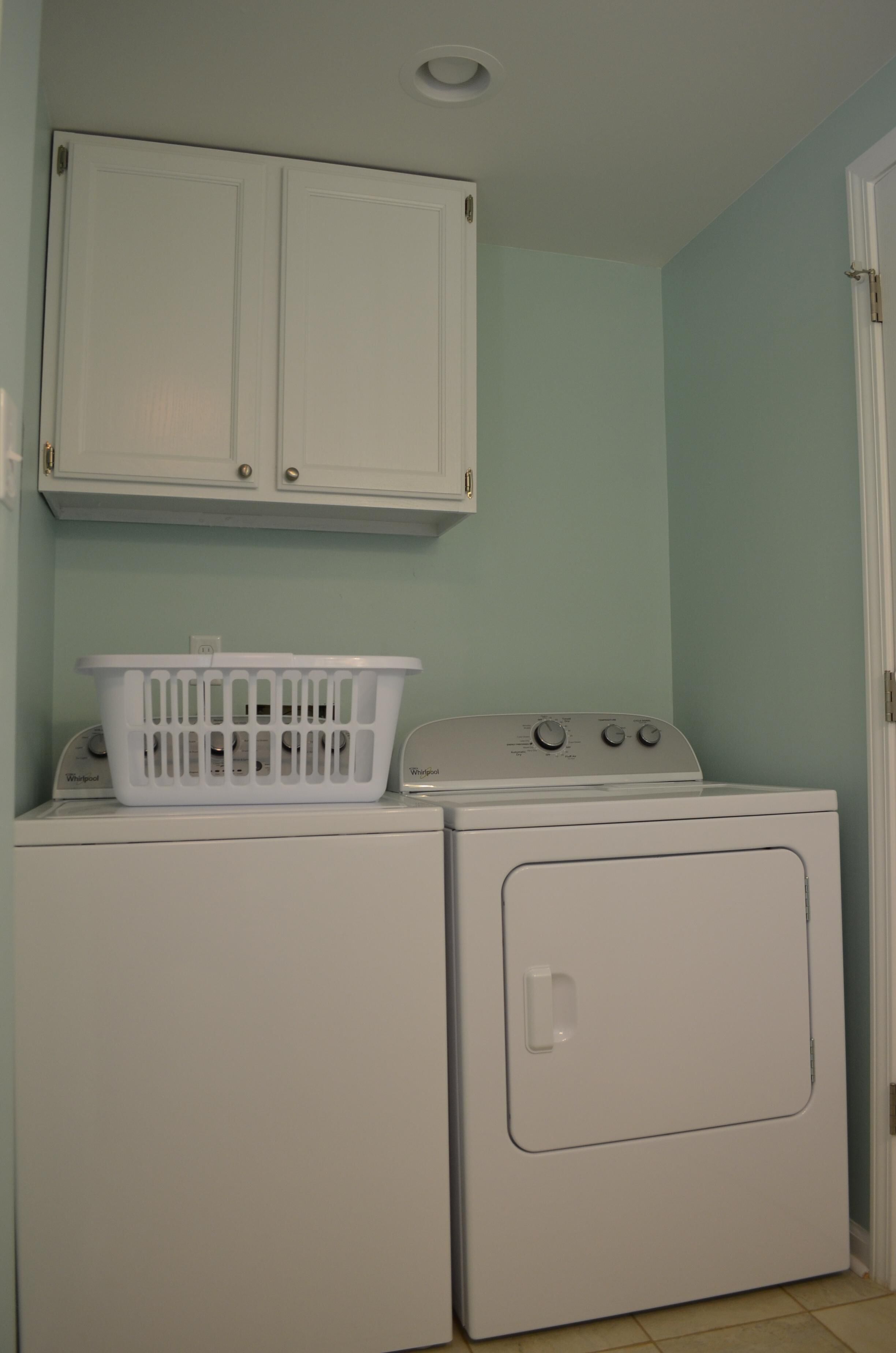 A laundry room with a washer and dryer, a white basket on the dryer, and a white cabinet above.