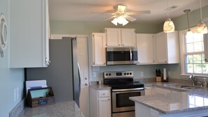 A kitchen with white cabinets, stainless steel appliances, granite countertops, and pendant lighting. - Oceanfront Cottage with Private Beach Access (Emerald Isle)