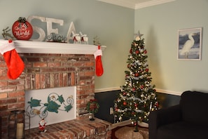 A cozy living room with a brick fireplace, a Christmas tree, and festive decorations.