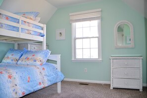 A room with bunk beds, a dresser, a window with blinds, and a mirror.
