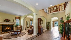A spacious living room with a fireplace, comfortable seating, and a grand staircase.