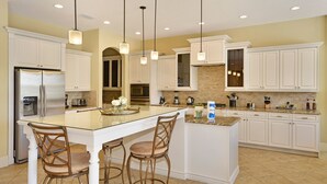 A spacious kitchen with white cabinetry, a central island with bar stools, stainless steel appliances, and pendant lighting.