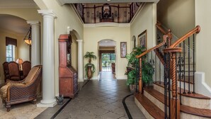 A grand hallway with a staircase, columns, and a piano.