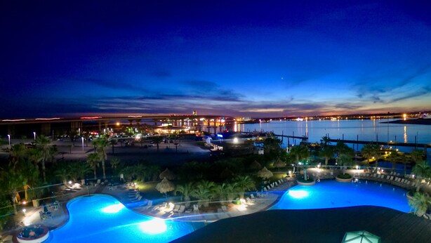 A resort pool area with multiple pools, palm trees, and a view of a marina at dusk. -  Gorgeous Sunsets!!  We now have some openings for first part of Aug.    (Orange Beach)