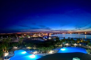 A resort pool area with multiple pools, palm trees, and a view of a marina at dusk. -  Gorgeous Sunsets!!  We now have some openings for first part of Aug.    (Orange Beach)