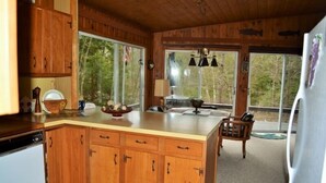A wooden cabin kitchen with a large island, wooden cabinets, and a view of the forest through the windows.