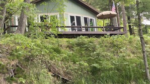 A cabin with a deck, surrounded by dense forest.