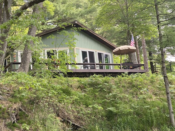 Una cabaña con terraza, rodeada de un bosque frondoso.