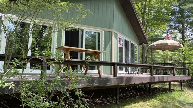 A rustic cabin with a deck, large windows, and an American flag.