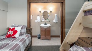 A bedroom with a bed, a wooden headboard, a nightstand, a dresser, a vanity with a mirror, and a bathroom with a sink and towel rack. - Convenient location on shuttle route with fantastic mountain views! (Park City)