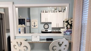 Cocina compacta con armarios blancos, microondas integrado y un pequeño comedor con dos sillas blancas.