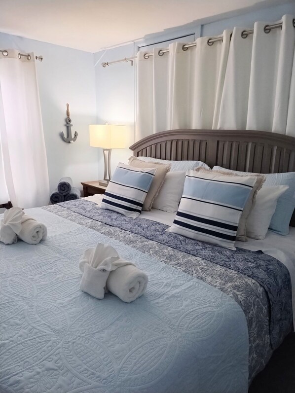 Una cama bien hecha con toallas enrolladas, una colcha estampada y almohadas a juego.