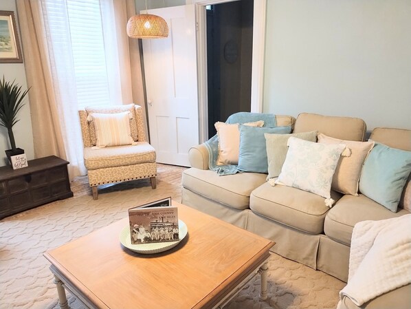 Un salon avec un canapé beige, une table basse en bois, un fauteuil à motifs et un lampadaire.