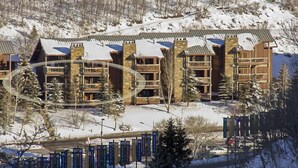 Ein mehrstöckiges Lodge mit Fassade aus Stein und Holz, Balkonen und einem verschneiten Berg im Hintergrund.