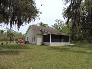 A single-story house with a covered porch, surrounded by a grassy yard and trees with Spanish moss.